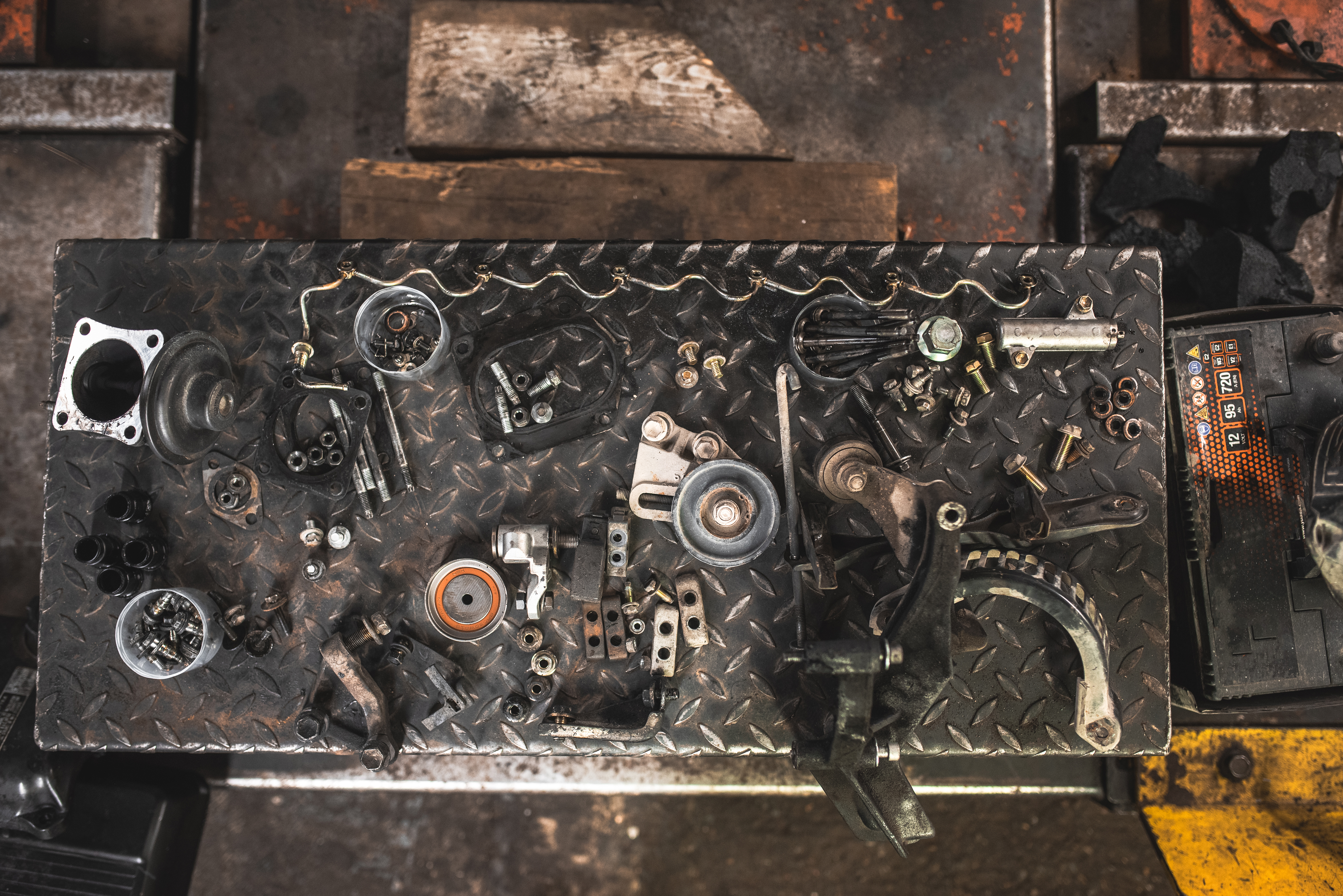 A collection of disassembled car components and hardware are neatly arranged on a diamond plate workbench, ready for repair or assembly